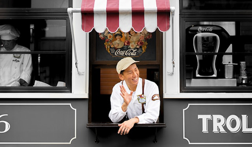 Restaurant worker hanging out of togo window smiling at customers.